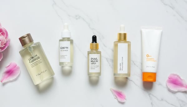 Korean Skip-Care minimalist flat lay — four K-beauty bottles on white marble with pink peony petals, editorial style